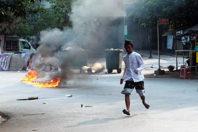 Un homme traverse la rue près d'une barricade en feu à Mandalay, en Birmanie, le 14 mars 2021 © AP