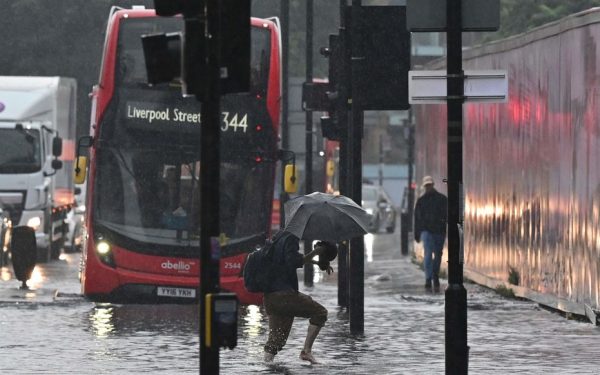 Un passant traverse une rue inondée de Londres après des pluies torrentielles © AFP/Justin Tallis 